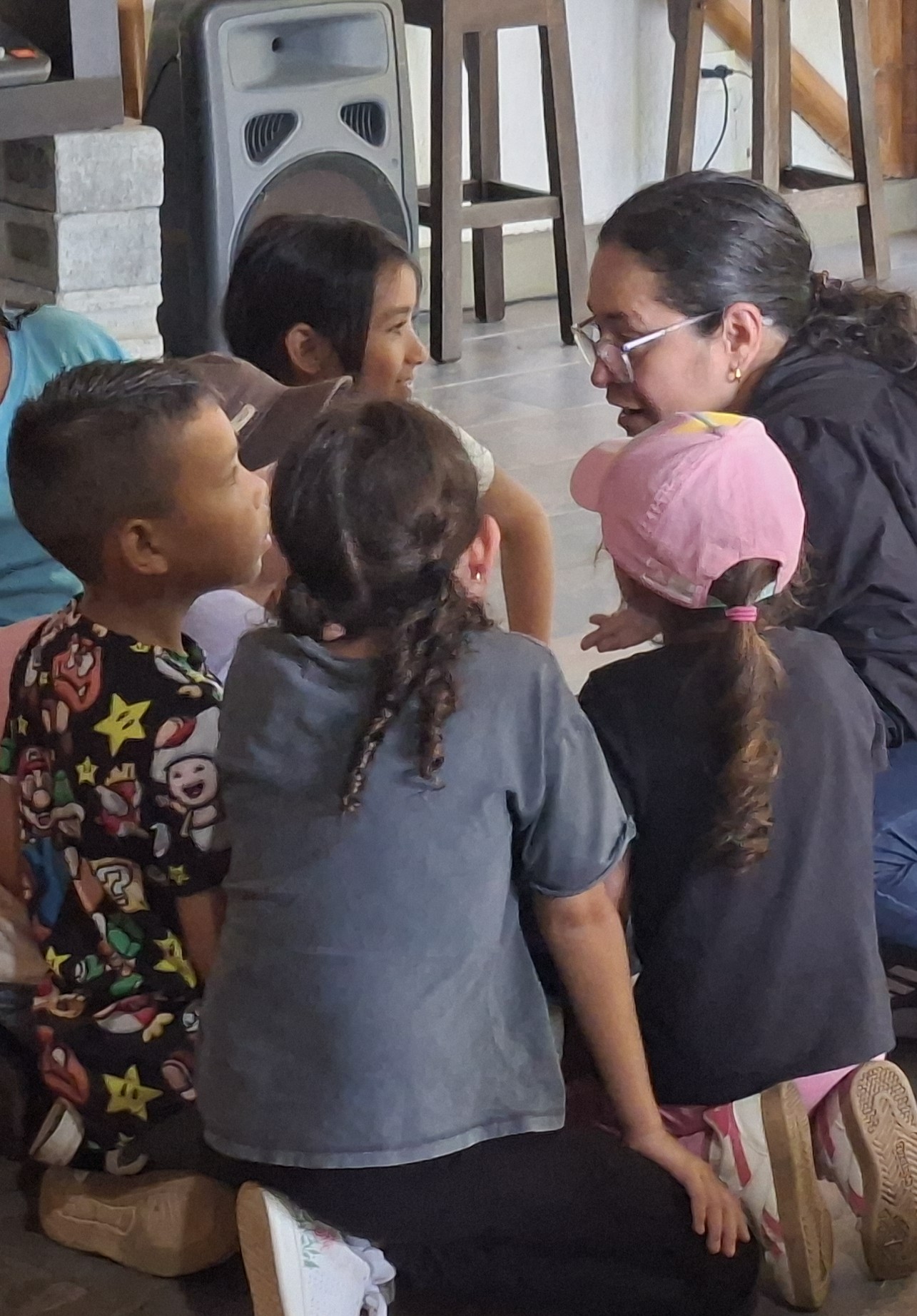 Niños, niñas y una maestra con gafas comparten en círculo en un espacio comunitario de La Buitrera
